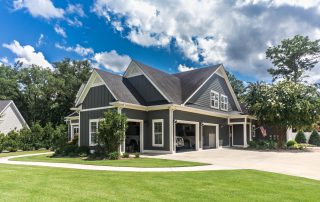 The side view of a large gray craftsman new construction house with a landscaped yard a three car garage and driveway. signs your garage door needs painting