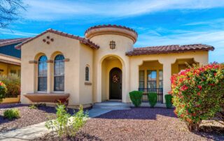 The image depicts a Spanish-style house with a terracotta tile roof and wrought iron detailing on the windows and doorway. how weather impacts exterior painting
