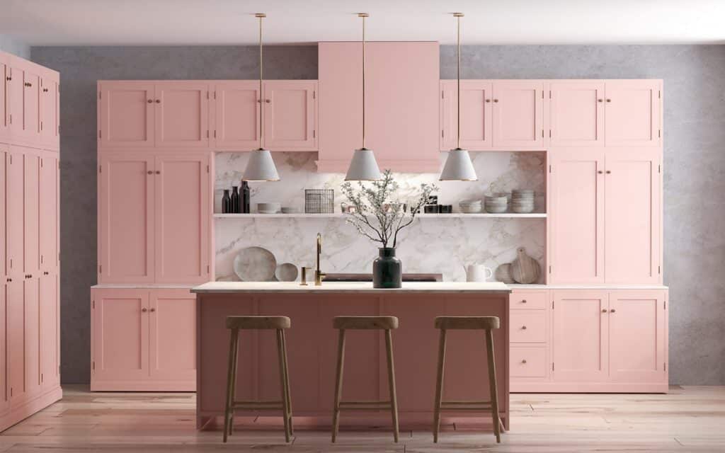 Pink-painted kitchen cabinets with white marble backsplash, island, pendant lights, and wood bar stools
